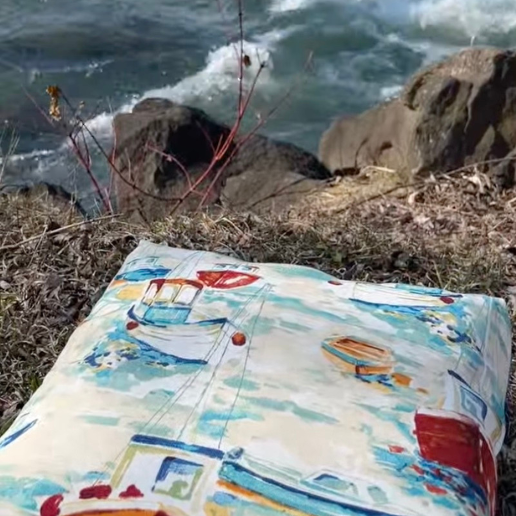 Colorful boat-patterned cushion on a rocky shore with waves in the background